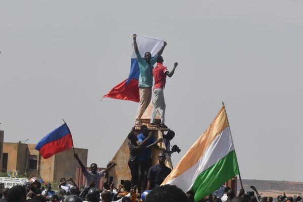 Протестующие размахивают нигерийскими и российскими флагами, собравшись во время митинга 30 июля 2023 года. Тысячи людей вышли на демонстрацию перед посольством Франции в Ниамее, после чего были разогнаны с применением слезоточивого газа. - Sputnik Таджикистан
