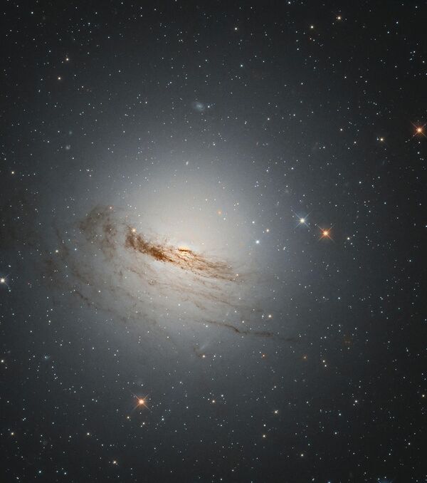 Необычная линзовидная галактика, известная как NGC 1947 расположена на расстоянии около 40 млн световых лет от Земли. На снимке видны слабые остатки спиральных рукавов галактики. Без большей части звездообразующего материала маловероятно, что в NGC 1947 родится много новых звезд, в результате чего эта галактика будет продолжать угасать со временем. - Sputnik Таджикистан