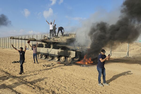 Палестинцы празднуют уничтожение израильского танка у забора сектора Газа к востоку от Хан-Юниса. Лидеры военного крыла ХАМАС в секторе Газа совершили беспрецедентную атаку с нескольких фронтов на Израиль, расстреливая тысячами ракет, когда десятки боевиков ХАМАС проникли через хорошо укрепленную границу в нескольких местах по воздуху, суше и морю и застали страну врасплох во время большого праздника. - Sputnik Таджикистан