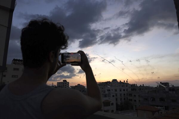 Мужчина записывает на свой мобильный телефон видео, на котором ракеты стреляют из города Газа в сторону Израиля. - Sputnik Таджикистан