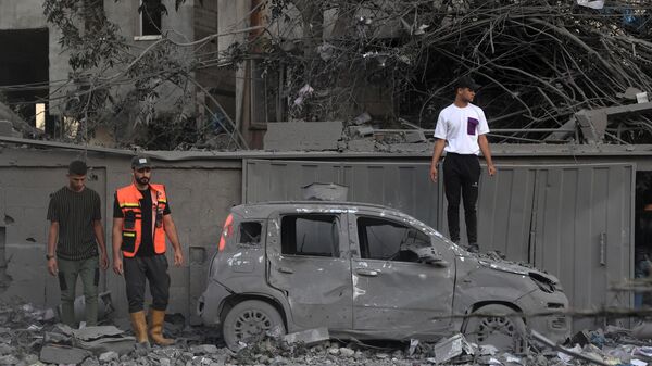 Спасатель и люди стоят возле сгоревшего автомобиля после израильского удара в Рафахе на юге сектора Газа - Sputnik Тоҷикистон