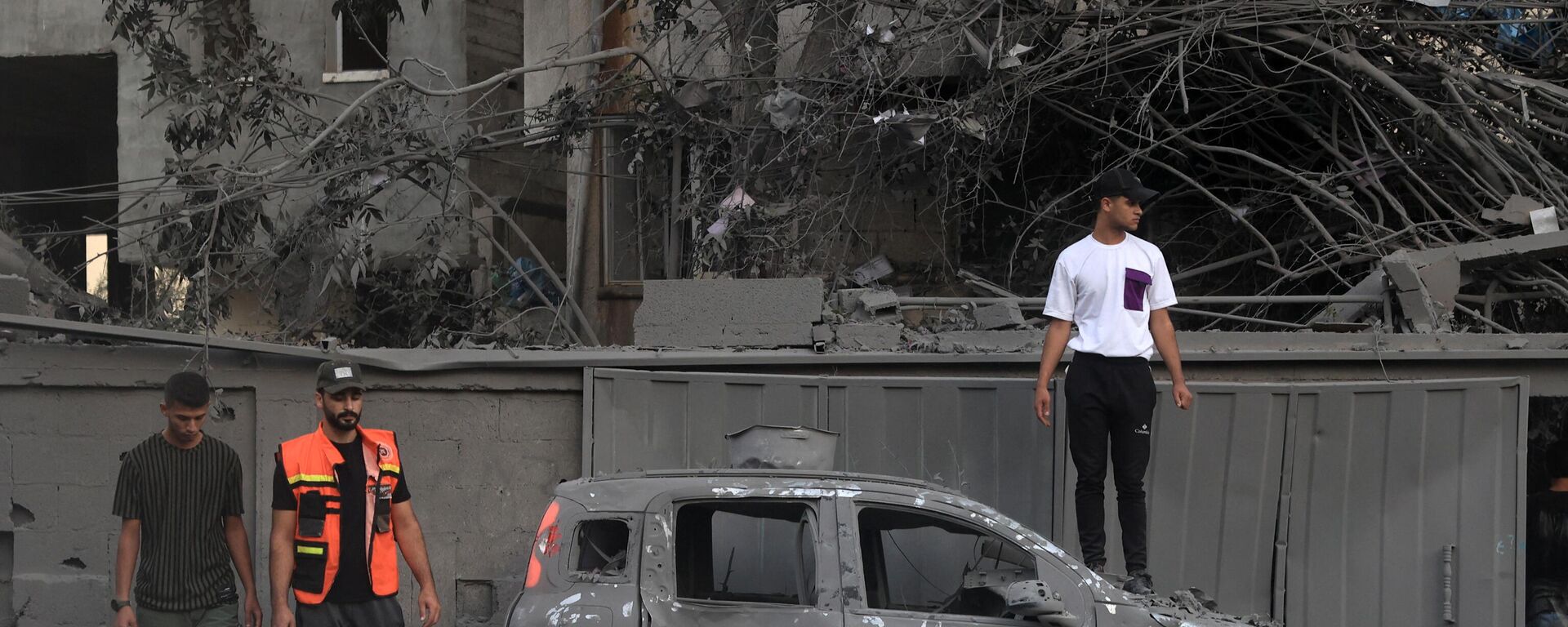 Спасатель и люди стоят возле сгоревшего автомобиля после израильского удара в Рафахе на юге сектора Газа - Sputnik Тоҷикистон, 1920, 18.10.2023