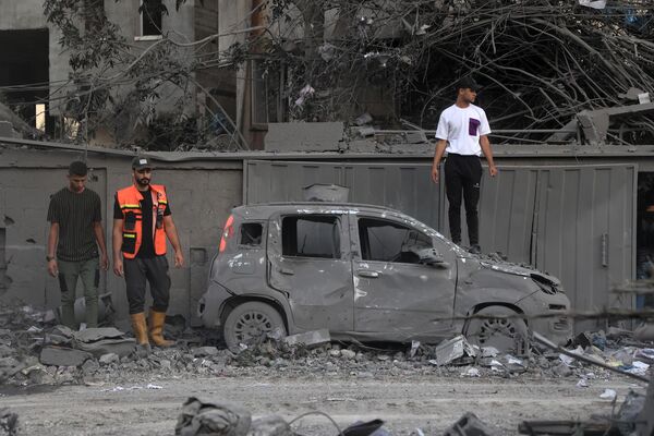 Спасатели и местные жители стоят возле сгоревшей машины после ракетных ударов на юге сектора Газа. - Sputnik Таджикистан