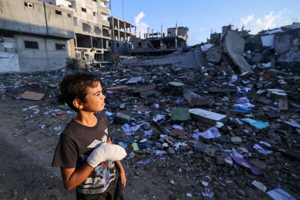 Раненый палестинский мальчик, 12-летний Мухаммад Софи, смотрит на разрушенное здание в лагере беженцев Рафах. - Sputnik Таджикистан