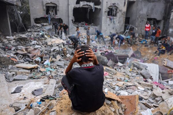 Ребенок реагирует на то, как люди спасают вещи среди обломков разрушенного здания после ударов по Рафаху на юге сектора Газа. - Sputnik Таджикистан