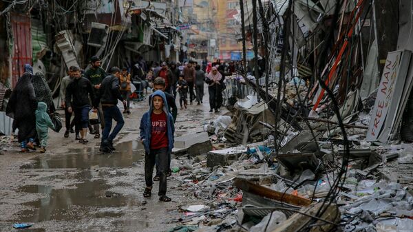 Палестинцы идут среди обломков зданий, пострадавших в результате израильских ударов, возле рынка Аль-Завия в городе Газа - Sputnik Тоҷикистон