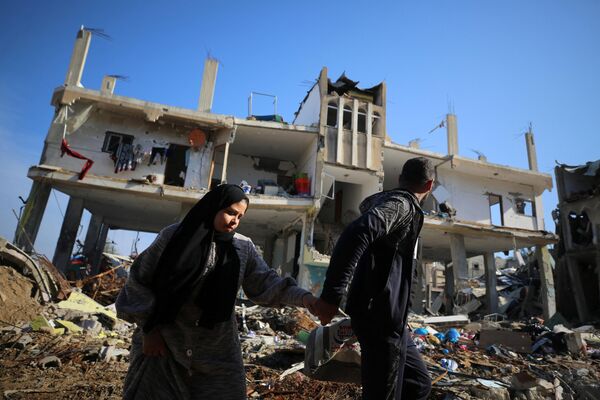 Палестинцы проходят мимо разрушенного здания в лагере беженцев Аль-Магази в центре сектора Газа. - Sputnik Таджикистан