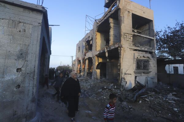 Палестинцы идут мимо жилого дома, разрушенного в результате израильского удара в Рафахе. - Sputnik Таджикистан