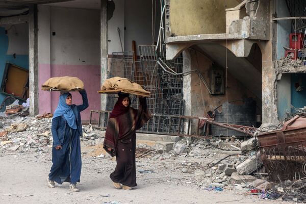 Женщины несут на головах буханки хлеба во время прогулки перед зданием, поврежденным в результате бомбардировки. - Sputnik Таджикистан