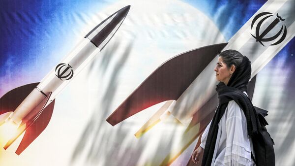Женщина проходит мимо баннера с изображением с эмблемой Исламской Республики Иран в центре Тегерана 15 апреля 2024 года  - Sputnik Таджикистан