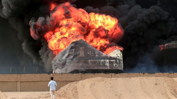 Мужчина стоит напротив бушующего огня в резервуарах для хранения нефти через день после израильских ударов по порту йеменского города Ходейда - Sputnik Тоҷикистон