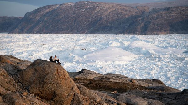 Студенты-исследователи из Нью-Йоркского университета сидят на скале, с которой открывается вид на ледник Хельхейм в Гренландии. - Sputnik Таджикистан