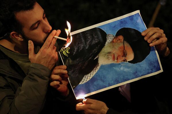 Як эътирозгар дар назди сафорати Эрон ҳангоми гирдиҳамоии пуштибонӣ аз эътирозҳои саросарии Эрон дар Лондон аз акси оташзадаи раҳбари олии Эрон Оятуллоҳ Алии Хоманаӣ сигор дармегиронад. - Sputnik Тоҷикистон