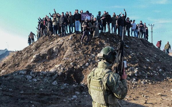 Турецкий солдат охраняет границу, в то время как прокурдские протестующие собираются на вершине холма, пытаясь пройти к приграничной зоне во время демонстрации в поддержку сирийских курдов и против недавних военных столкновений между сирийской армией и курдскими силами в Нусайбине, на юго-востоке Турции. - Sputnik Таджикистан