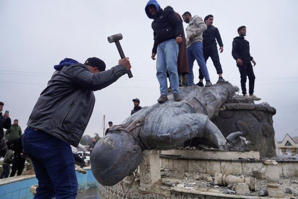 Як гурӯҳ аз шаҳрвандон дар шаҳри Табқа муҷассамаи як ҷангҷӯи Нерӯҳои Демократии Сурияро пас аз он ки артиши Сурия онро таҳти назорат гирифт, шикастанд. - Sputnik Тоҷикистон