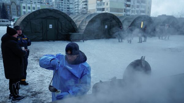 Сотрудник Государственной службы по чрезвычайным ситуациям наливает чай в чашку перед палатками правительственного пункта гуманитарной помощи. Киев, Украина, 25 января 2026 года. - Sputnik Таджикистан