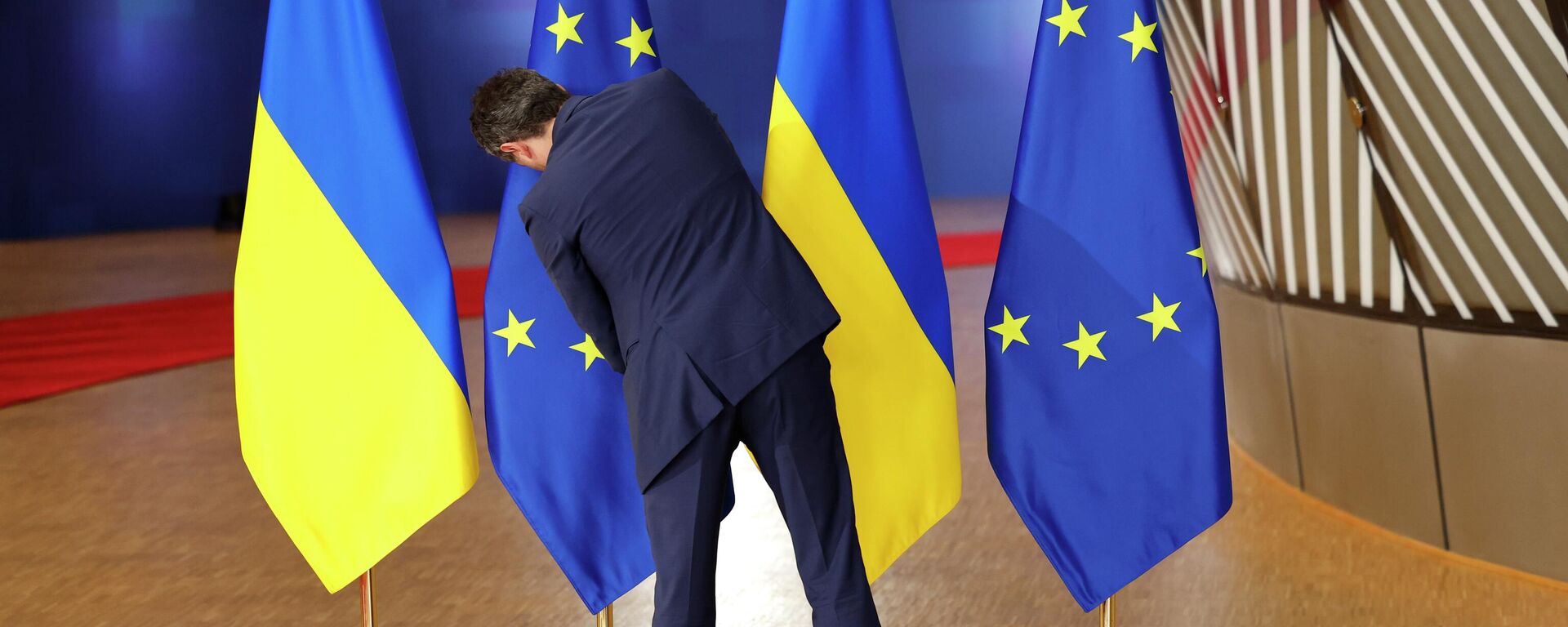 Сотрудник протокола поправляет флаги ЕС и Украины во время саммита ЕС в Брюсселе. Архивное фото - Sputnik Таджикистан, 1920, 19.02.2026