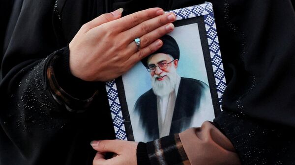 Женщина держит в руках портрет верховного лидера Ирана аятоллы Али Хаменеи на площади Энгелаб, погибшего в результате израильских и американских ударов в субботу в Тегеране, Иран, 1 марта 2026 года.  - Sputnik Тоҷикистон