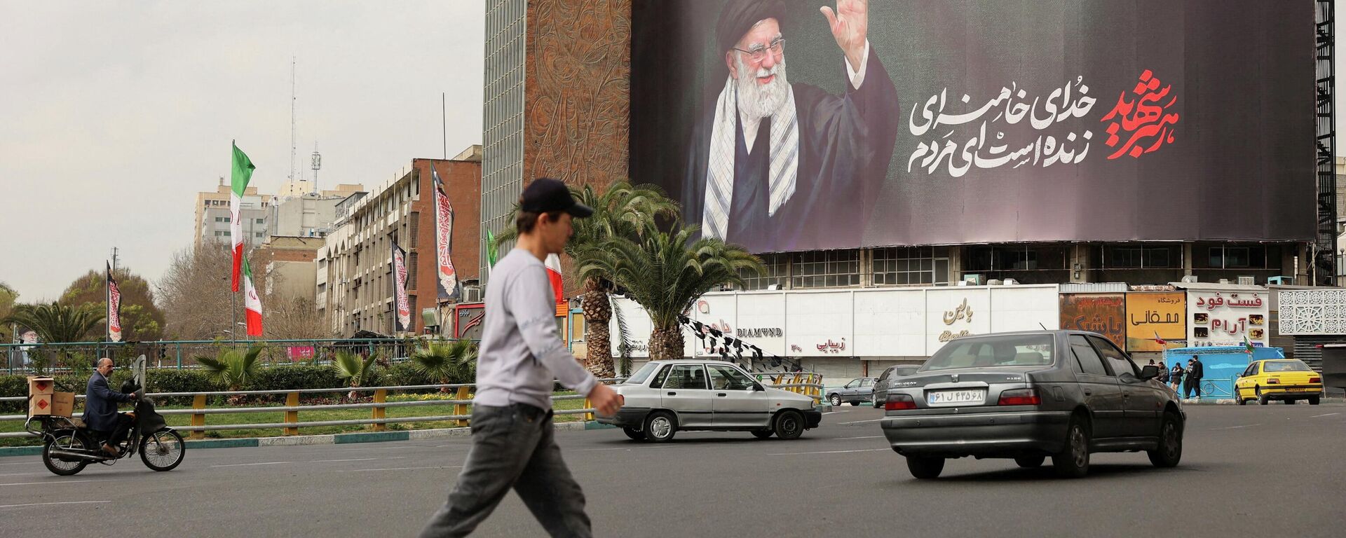 Люди идут мимо рекламного щита с изображением покойного верховного лидера Ирана аятоллы Али Хаменеи в Тегеране, Иран, 2 марта 2026 года. - Sputnik Таджикистан, 1920, 02.03.2026