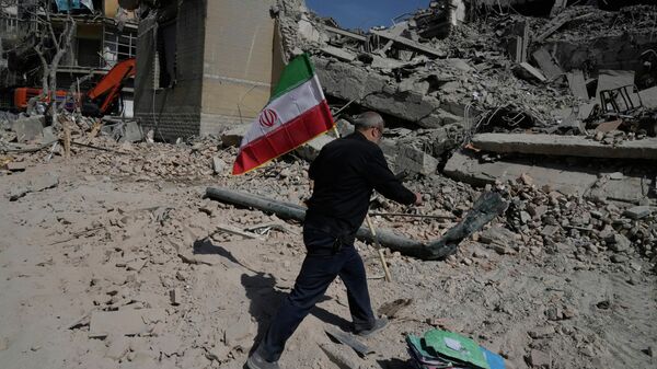 Мужчина несёт иранский флаг, чтобы положить его на обломки полицейского участка, пострадавшего во время американо-израильского удара в Тегеране, Иран, среда, 4 марта 2026 года.  - Sputnik Таджикистан