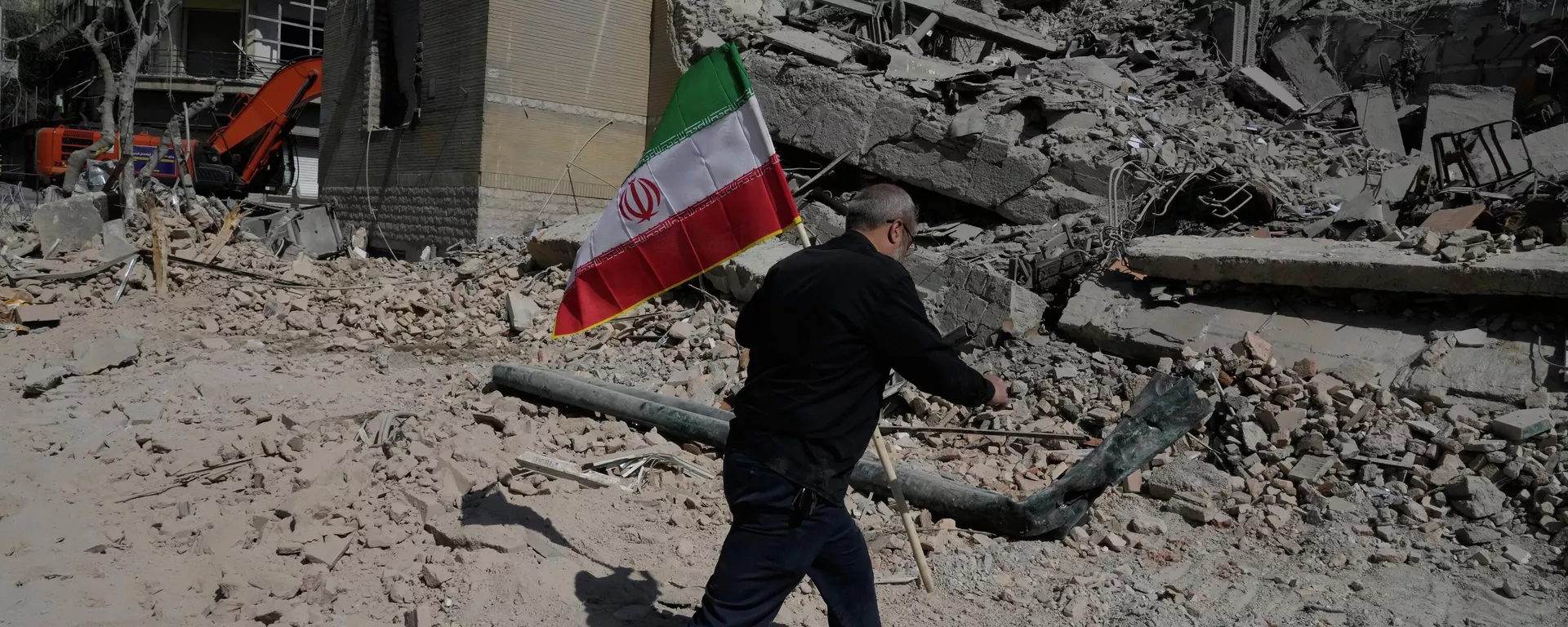 Мужчина несёт иранский флаг, чтобы положить его на обломки полицейского участка, пострадавшего во время американо-израильского удара в Тегеране, Иран, среда, 4 марта 2026 года.  — Sputnik Таджикистан, 1920, 06.03.2026