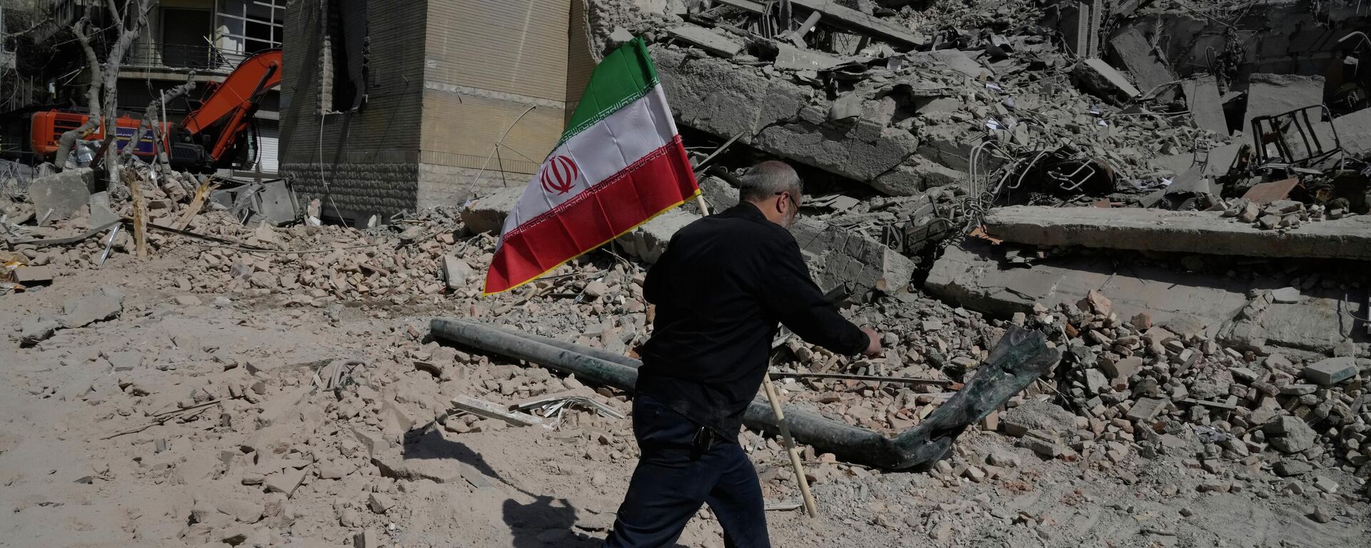Мужчина несёт иранский флаг, чтобы положить его на обломки полицейского участка, пострадавшего во время американо-израильского удара в Тегеране, Иран, среда, 4 марта 2026 года.  - Sputnik Таджикистан, 1920, 06.03.2026
