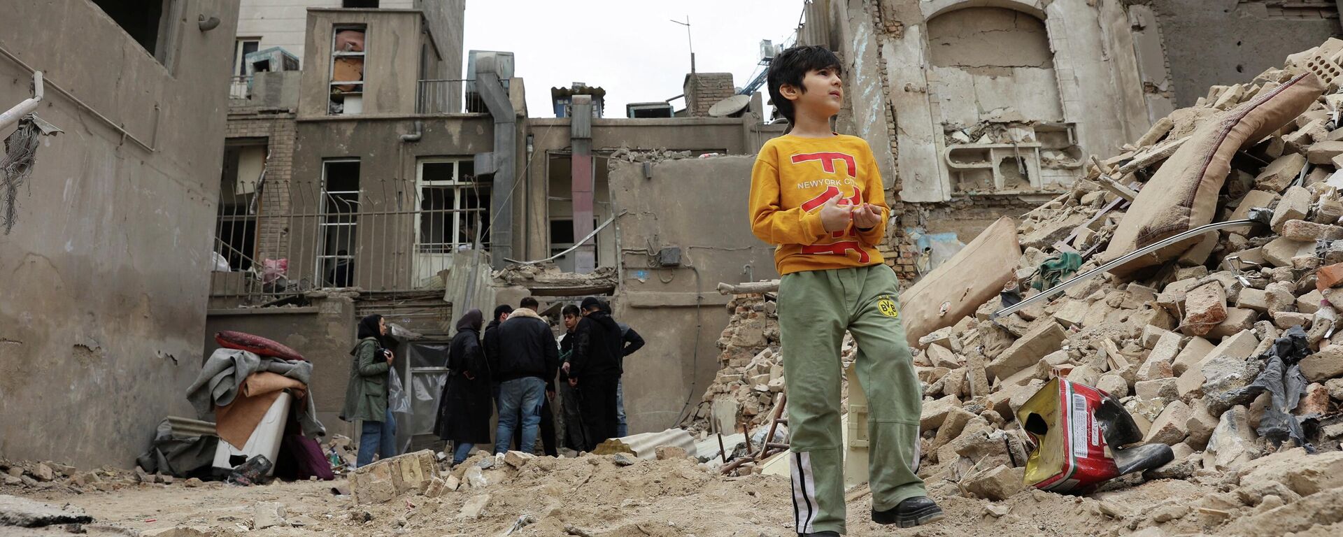 Мальчик стоит возле дома, поврежденного в результате удара, на фоне американо-израильского конфликта с Ираном, в Тегеране, Иран, 15 марта 2026 года.  - Sputnik Тоҷикистон, 1920, 16.03.2026