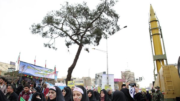 Иранцы на митинге, посвященном 37-й годовщине исламской революции, рядом с баллистической ракетой класса земля-земля большой дальности Emad в Тегеране, Иран - Sputnik Таджикистан