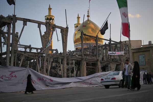 Пиёдагардон аз назди бинои харобшуда назди масҷиди Ҳусайн мегузаранд. Масҷид дар пасманзар намоён аст. Ба гуфтаи мақомот, ин иншоот рӯзи 4 апрели соли 2026, дар Занҷони Эрон, зери ҳамлаҳои ҳавоии ИМА ва Исроил қарор гирифтааст - Sputnik Тоҷикистон