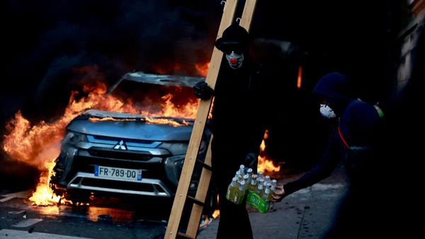 Участник беспорядков проходит мимо горящего автомобиля во время акции протеста против повышения стоимости жизни и цен на топливо в Париже, Франция - Sputnik Таджикистан