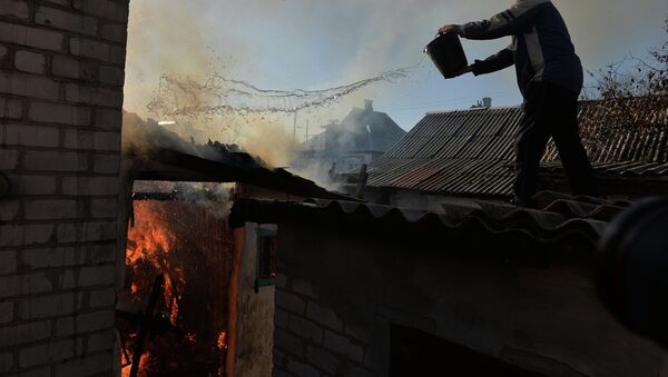 Житель Донецка тушит горящий огонь в доме, пострадавшем во время артиллерийского обстрела. Архивное фото - Sputnik Таджикистан