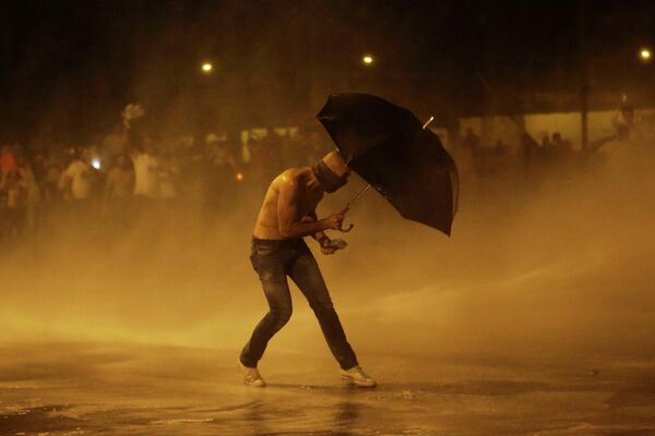 Протестующий защищается зонтом от водометов во время акции протеста в Бейруте (Ливан) - Sputnik Таджикистан