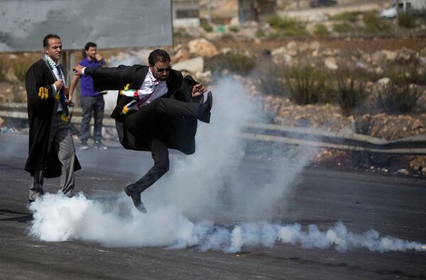 Протестующий пинает банку со слезоточивым газом во время столкновений местного населения с израильскими военными и полицейскими в провинции Рамалла - Sputnik Таджикистан