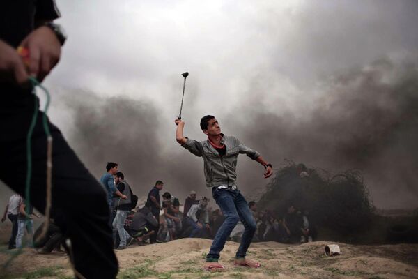 Палестинский протестующий использует пращу в процессе столкновения с израильской полицией в секторе Газа - Sputnik Таджикистан