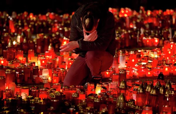 Мужчина сидит среди зажженных свечей в память о жертвах пожара, произошедшего в ночном клубе Бухареста (Румыния) - Sputnik Таджикистан