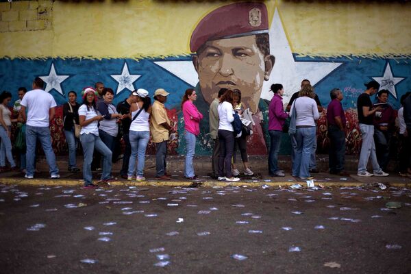 Люди стоят у стены с портретом Уго Чавеса во время выборов в конгресс в городе Каракас (Венесуэла) - Sputnik Таджикистан