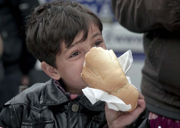 Мальчик ест буханку хлеба во время благотворительного обеда для бездомных возле главного вокзала в Бухаресте - Sputnik Таджикистан