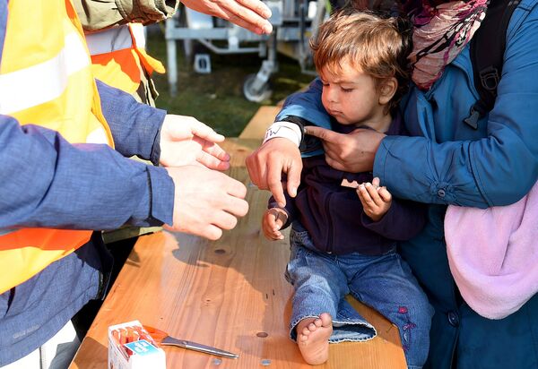 Мигрант с ребенком по прибытию в Европу получает наручный браслет.  Архивное фото - Sputnik Таджикистан