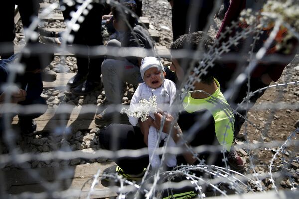 Мигрант держит ребенка  в деревне Идомени (Греция) возле македонско-греческой границы - Sputnik Таджикистан