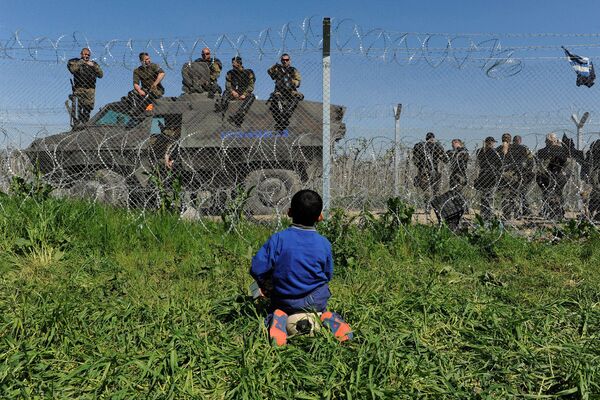 Мальчик из лагеря беженцев смотрит на македонских полицейских в районе греческо-македонской границы - Sputnik Таджикистан