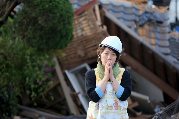 Женщина стоит рядом с развалами дома в городе Машики (Япония) после разрушительного землетрясения - Sputnik Таджикистан