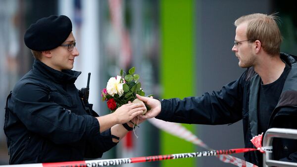 Люди приносят цветы к торговому комплексу в Мюнхене, где неизвестный убил 9 человек - Sputnik Таджикистан