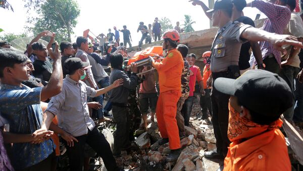 Спасатели и сотрудники полиции на месте разрушенного в результате землетрясения здания в Индонезии - Sputnik Таджикистан