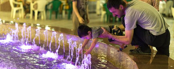 Мужчина играет у фонтана с ребенком, архивное фото - Sputnik Тоҷикистон