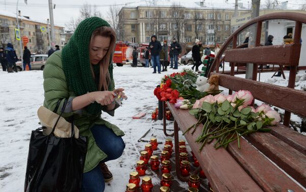 Женщина зажигает свечу возле здания торгового центра  Зимняя вишня в Кемерове, где произошел пожар - Sputnik Таджикистан