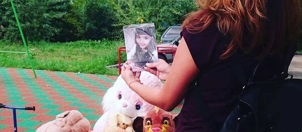 Девушка держит фотографию убитой девочки на мемориале - Sputnik Таджикистан