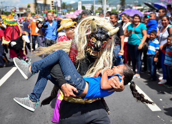 Человек в маске мифологического существа держит на руках девочку во время парада в Сан-Сальвадоре - Sputnik Таджикистан