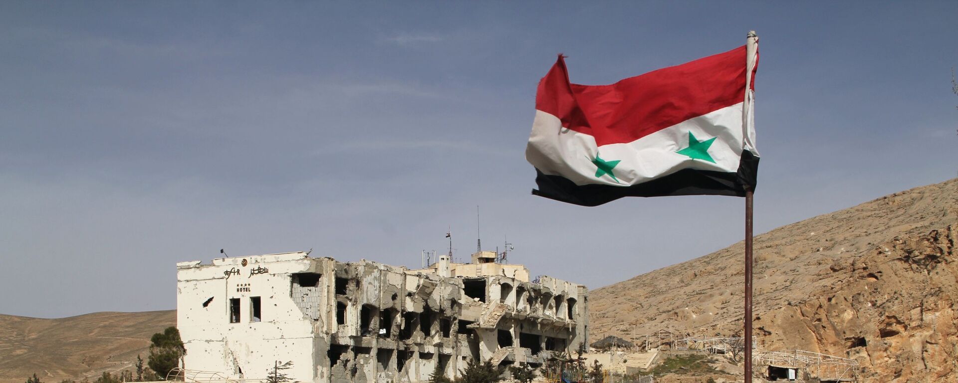 Сирийский флаг на фоне разрушенного дома в сирийском городе Маалюля - Sputnik Таджикистан, 1920, 28.03.2021