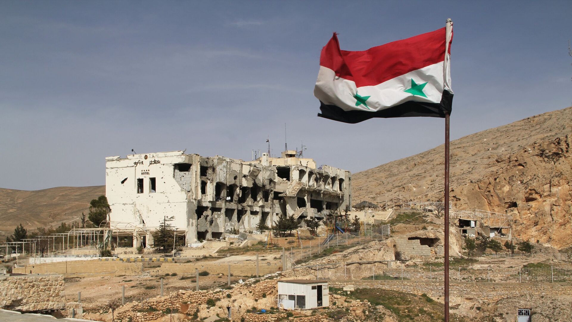 Сирийский флаг на фоне разрушенного дома в сирийском городе Маалюля - Sputnik Таджикистан, 1920, 26.02.2021