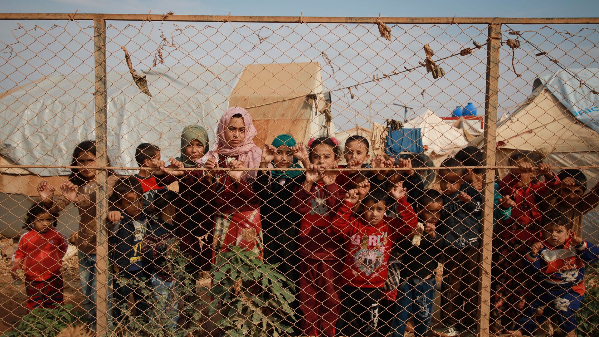 Сирийские дети у забора палаточного лагеря недалеко от деревни Кафр-Лусин, Сирия - Sputnik Тоҷикистон, 1920, 25.07.2022